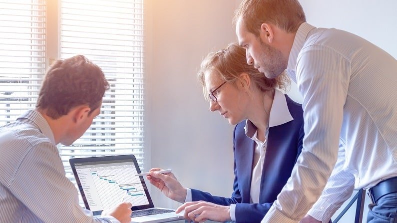 Accueil project manager meeting with team for decision on planning milestones and deliverables, gantt chart schedule on computer screen, 3 people in office